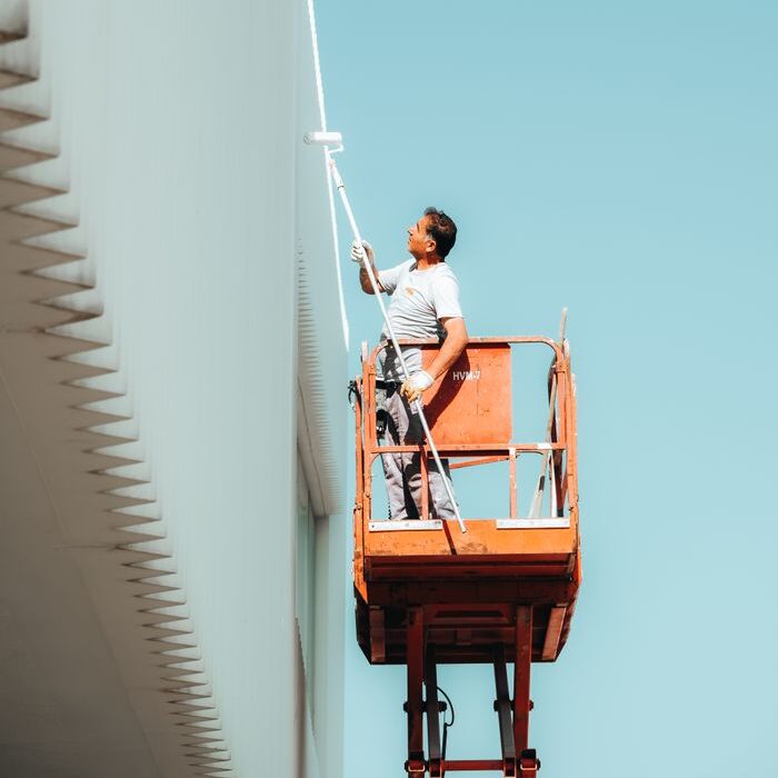 A man painting a building exterior from a cherry picker against a clear blue sky.
