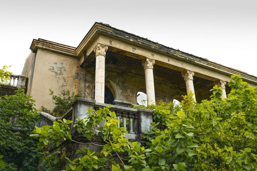 An old abandoned villa in Tskaltubo, Georgia, enveloped by lush greenery, showcasing classical architecture.