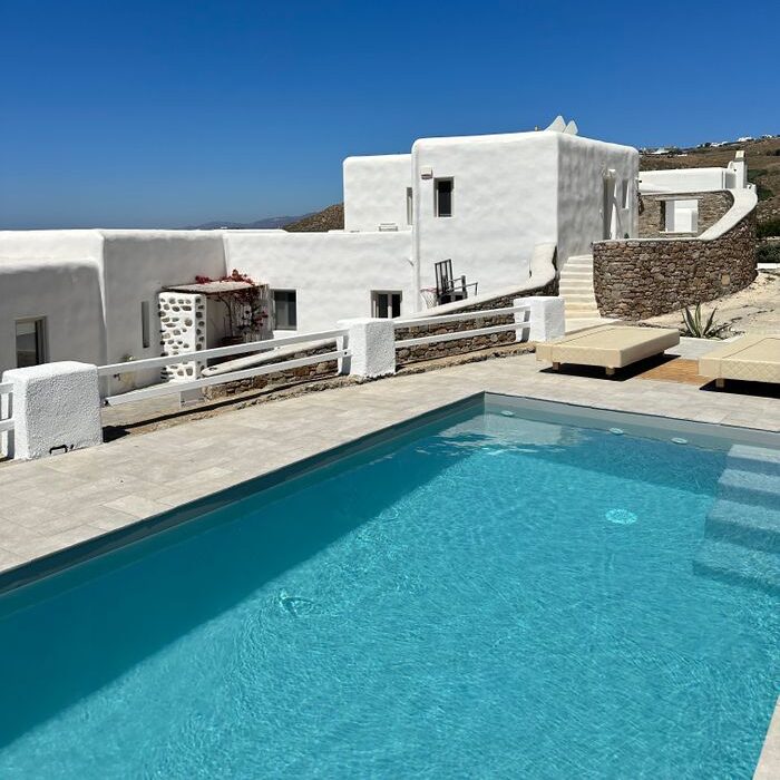 Bright Greek architecture and pool under clear blue sky in Mykonos, Greece.