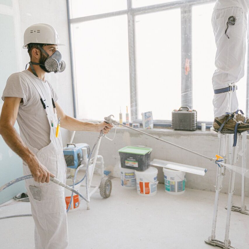 Two construction workers wearing protective gear and painting interior walls for a renovation project.