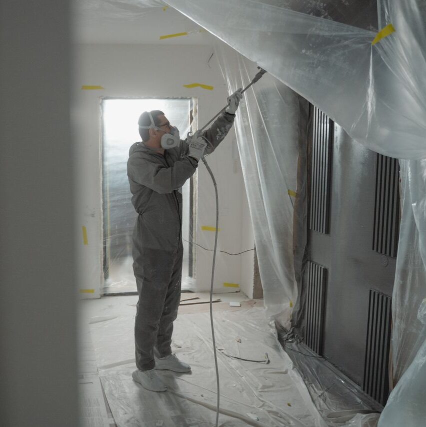 Man in protective gear spray painting a house's interior during renovation work.